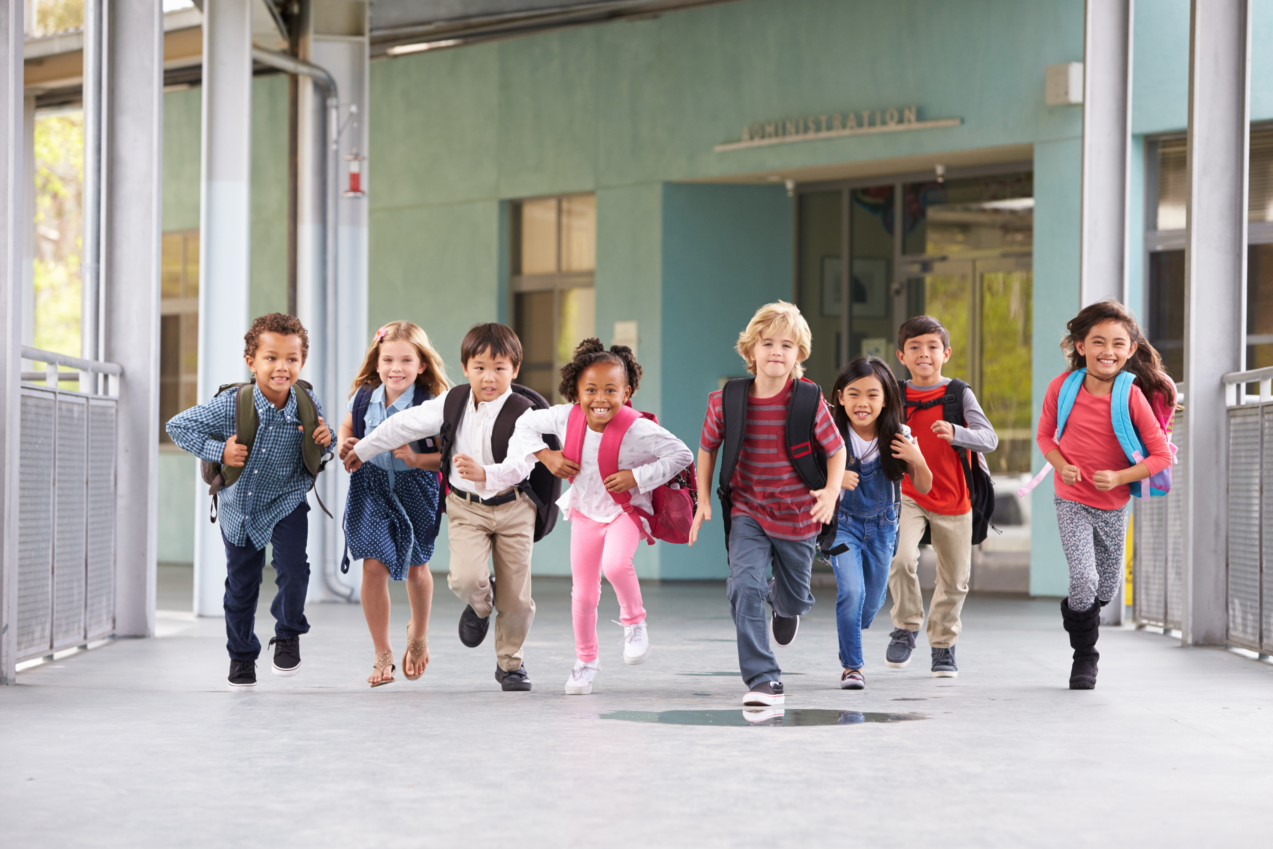 Eine Gruppe aufgeregter Grundschulkinder mit Rucksäcken rennt einen hellen Flur entlang. Grundschule „Bjarnat Krawc“ Königswartha.